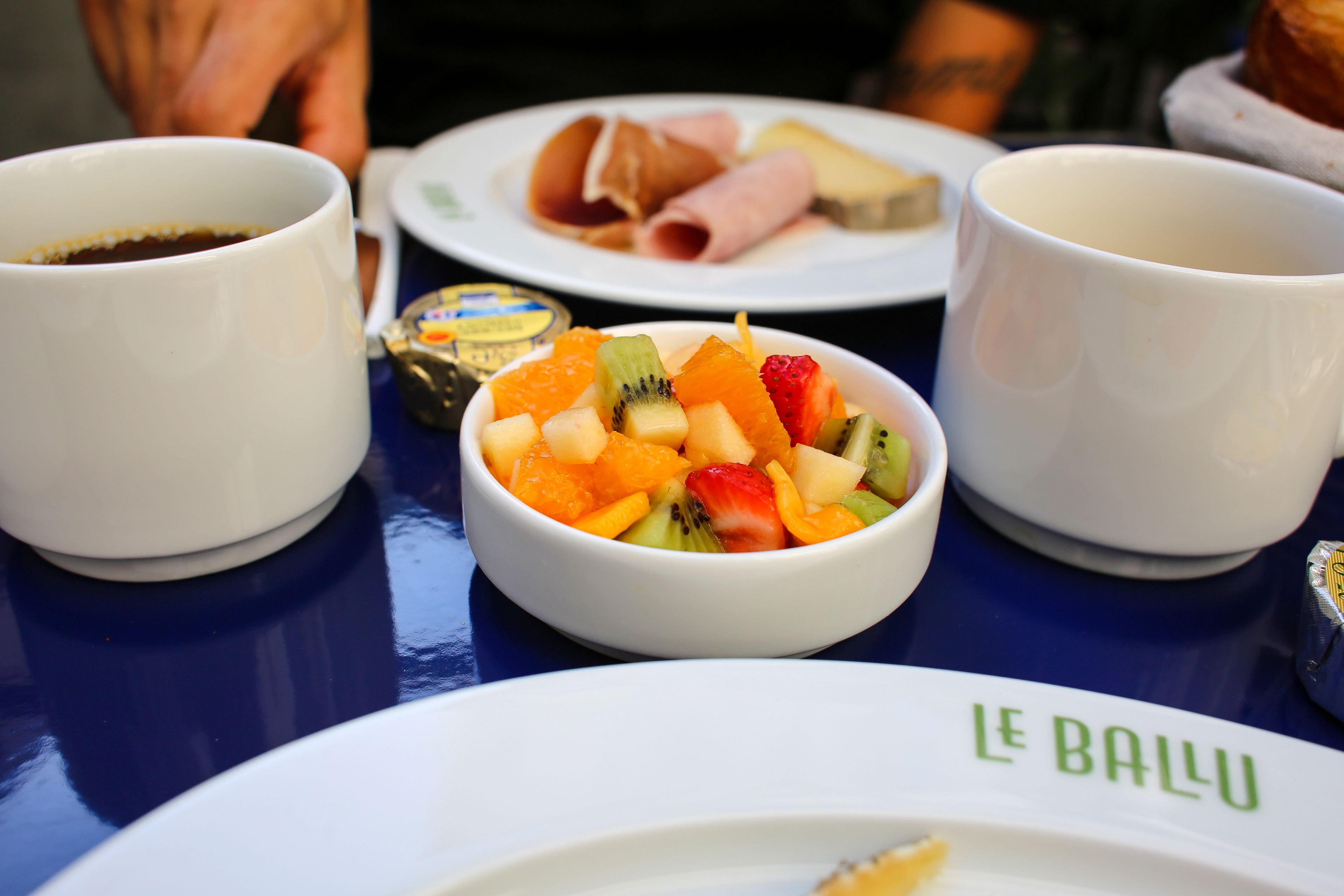 A table with a white plate labeled "LE BALU" and a bowl of fruit salad.