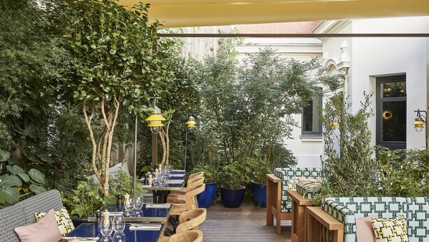 An outdoor patio with wooden tables and chairs, surrounded by lush greenery and potted plants. - Hotel Le Ballu (Paris)