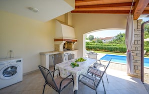 A patio with a table set for four, a washing machine, and a pool in the background. - Stunning home in Kmacici (Kmacici)