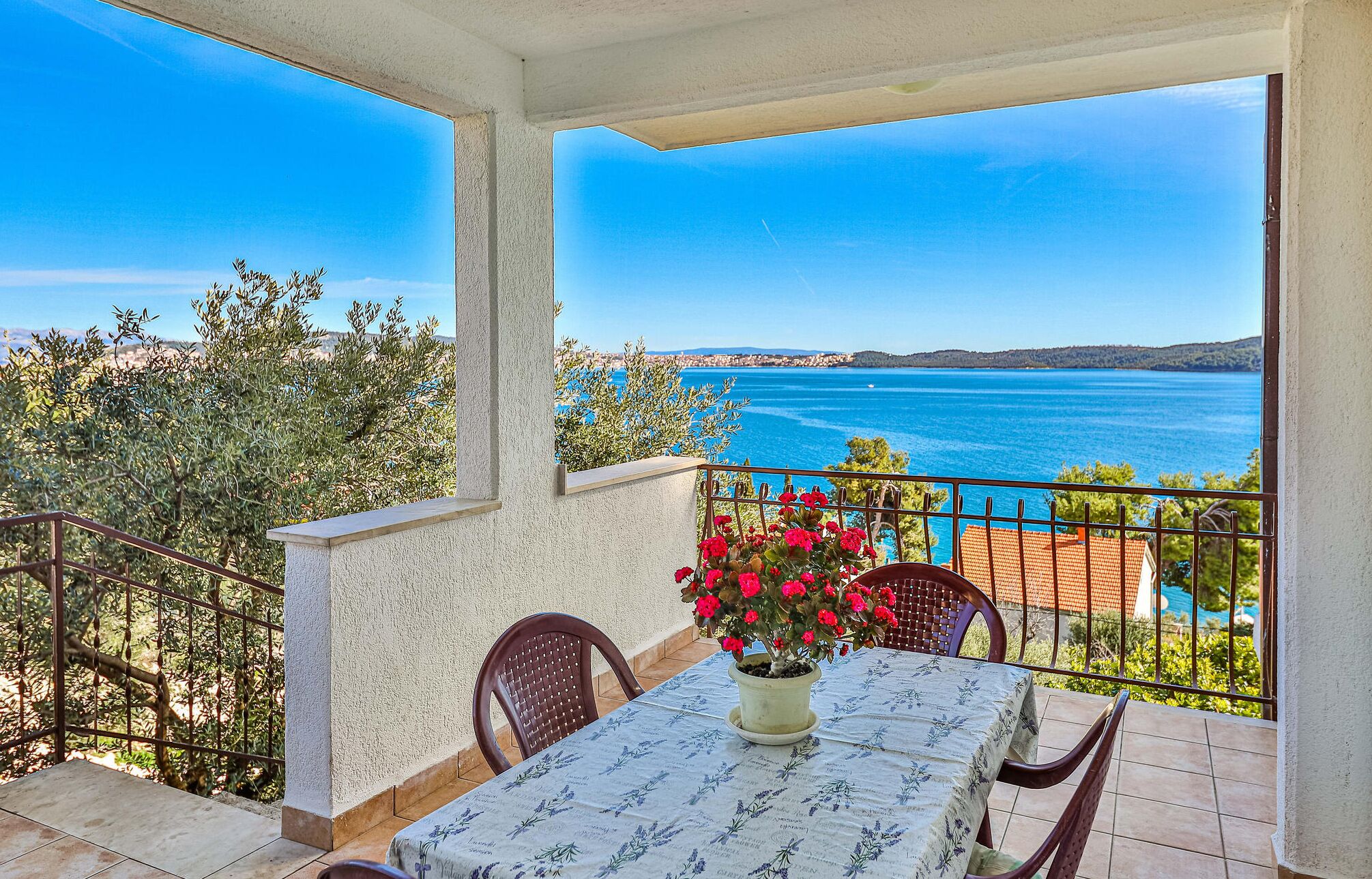 Un balcon avec une table et des chaises, offrant une vue sur la côte et un ciel dégagé.