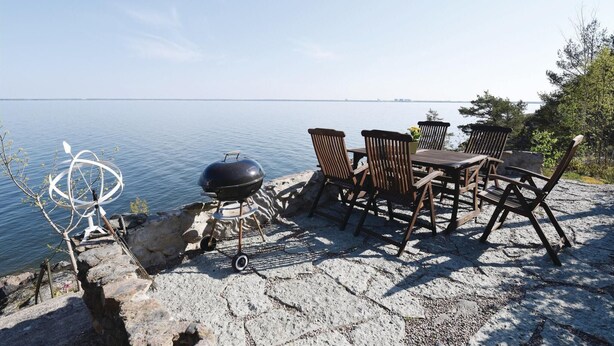 A seaside patio with a grill, chairs, and a table overlooking the water. - Nice home in Lidköping with kitchen (Lidköping)