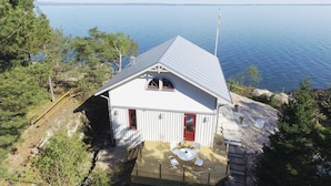 A small cabin with a red door, white walls, and a sloped roof overlooking a body of water. - Nice home in Lidköping with kitchen (Lidköping)