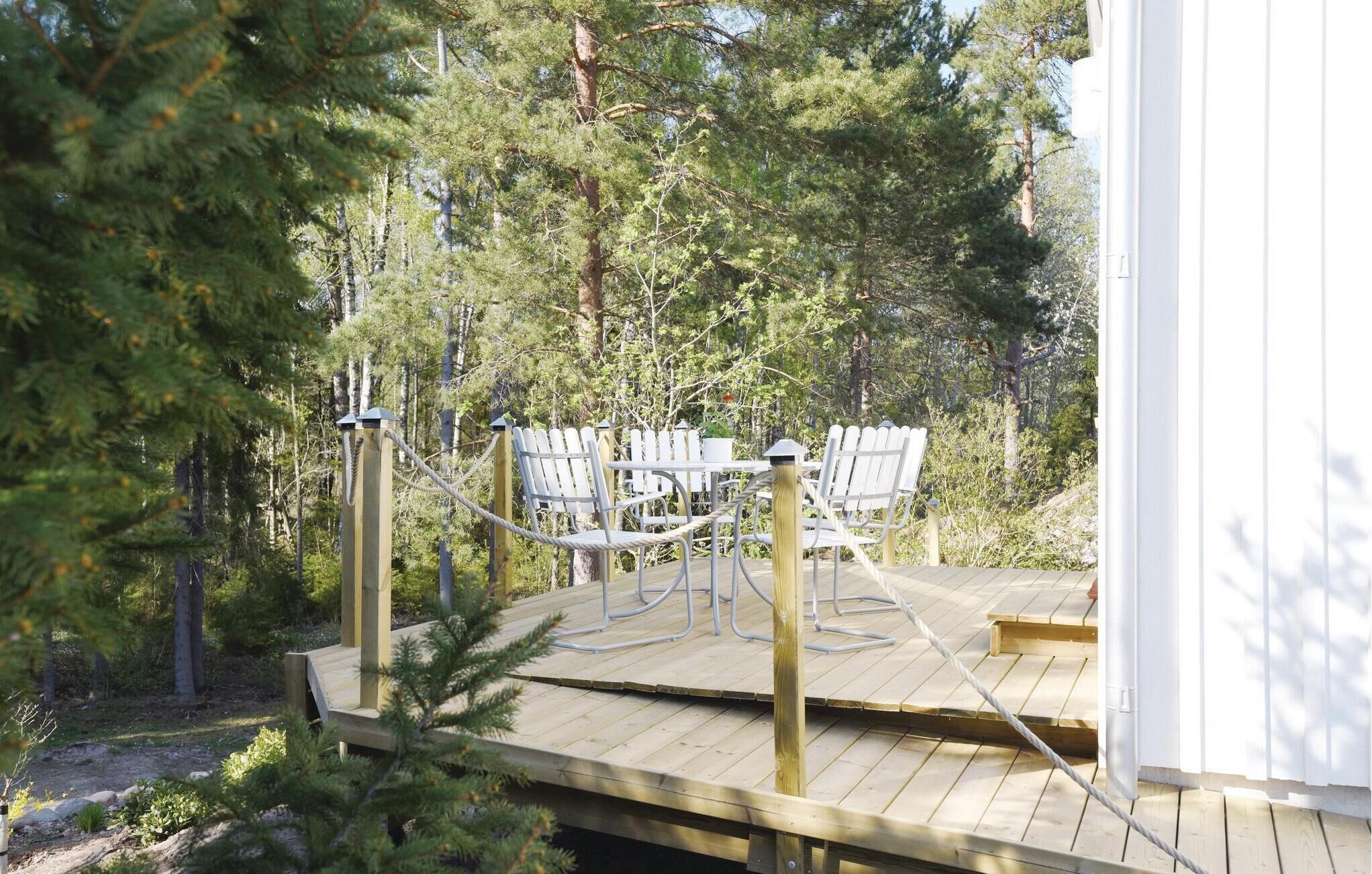 A wooden deck with white chairs and a rope barrier, surrounded by trees.