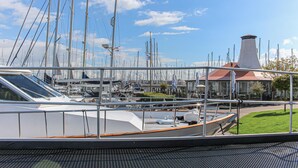 A marina with multiple sailboats docked, a building with a red roof, and a grassy area in the background.