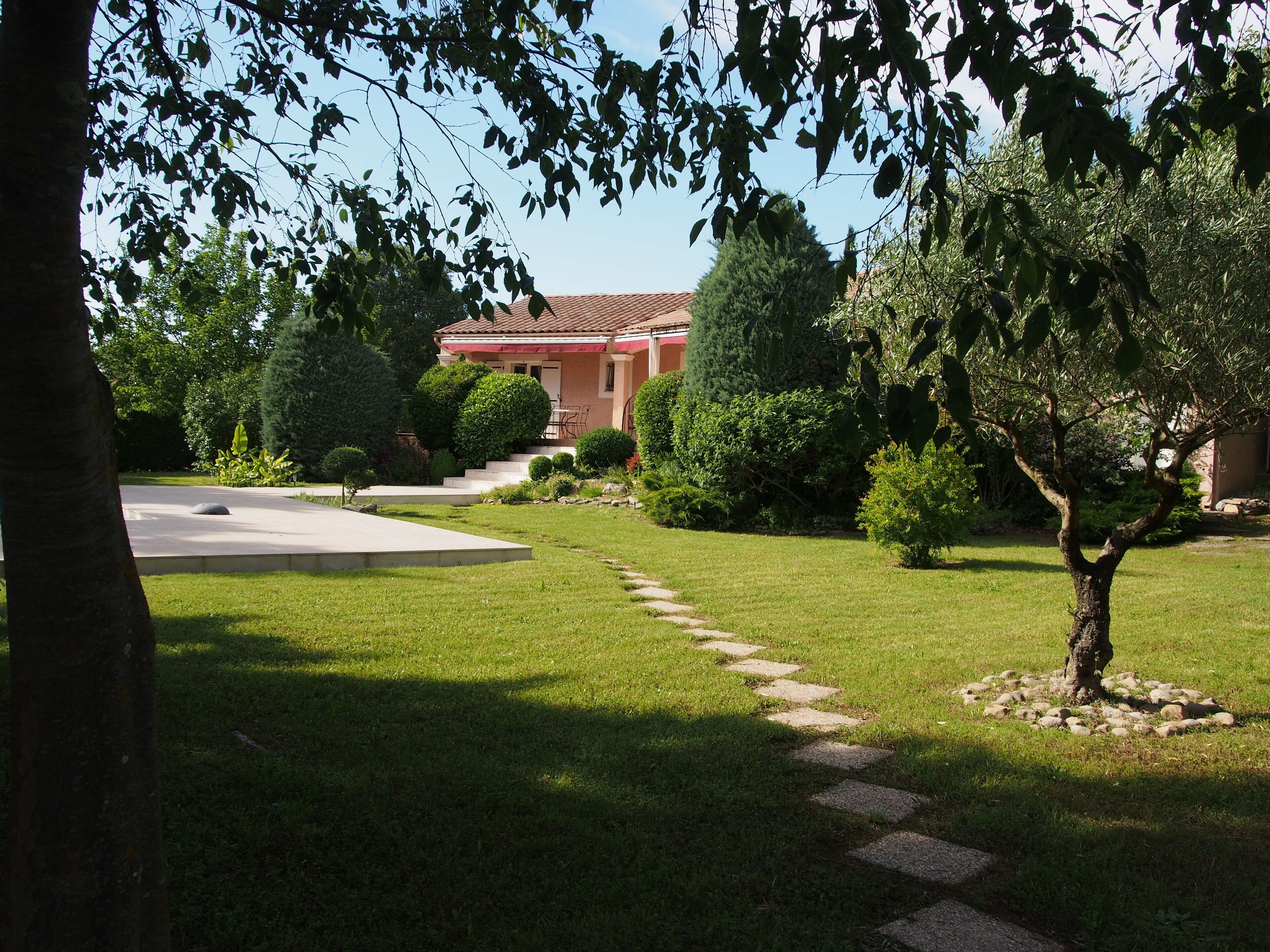 A well-maintained garden with a paved pathway leading to a building with a red roof.