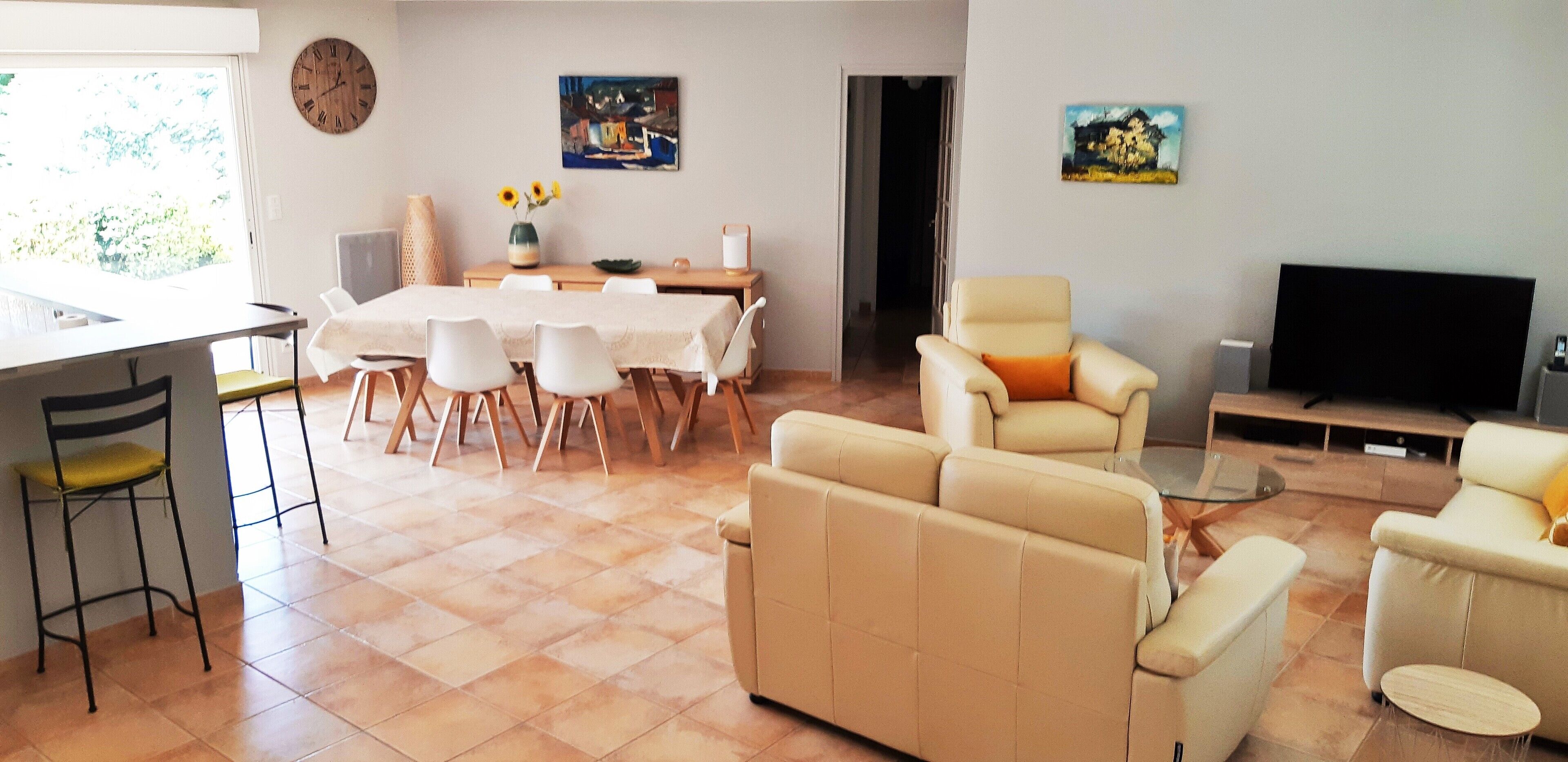 Ein Wohnzimmer mit einer Couch, Sesseln, einem Fernseher und einem Essbereich mit Tisch und Stühlen.