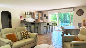 Ein modernes Wohnzimmer mit einer Couch, Sesseln und einem Couchtisch. Es gibt eine Küchenzeile mit Barhocker und einem Esstisch.