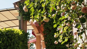 Ein überdachter Außenbereich mit einer Steinsäule, Stufen, die zu einem überdachten Eingang führen, und üppigem Grün, darunter eine Rosenpflanze.