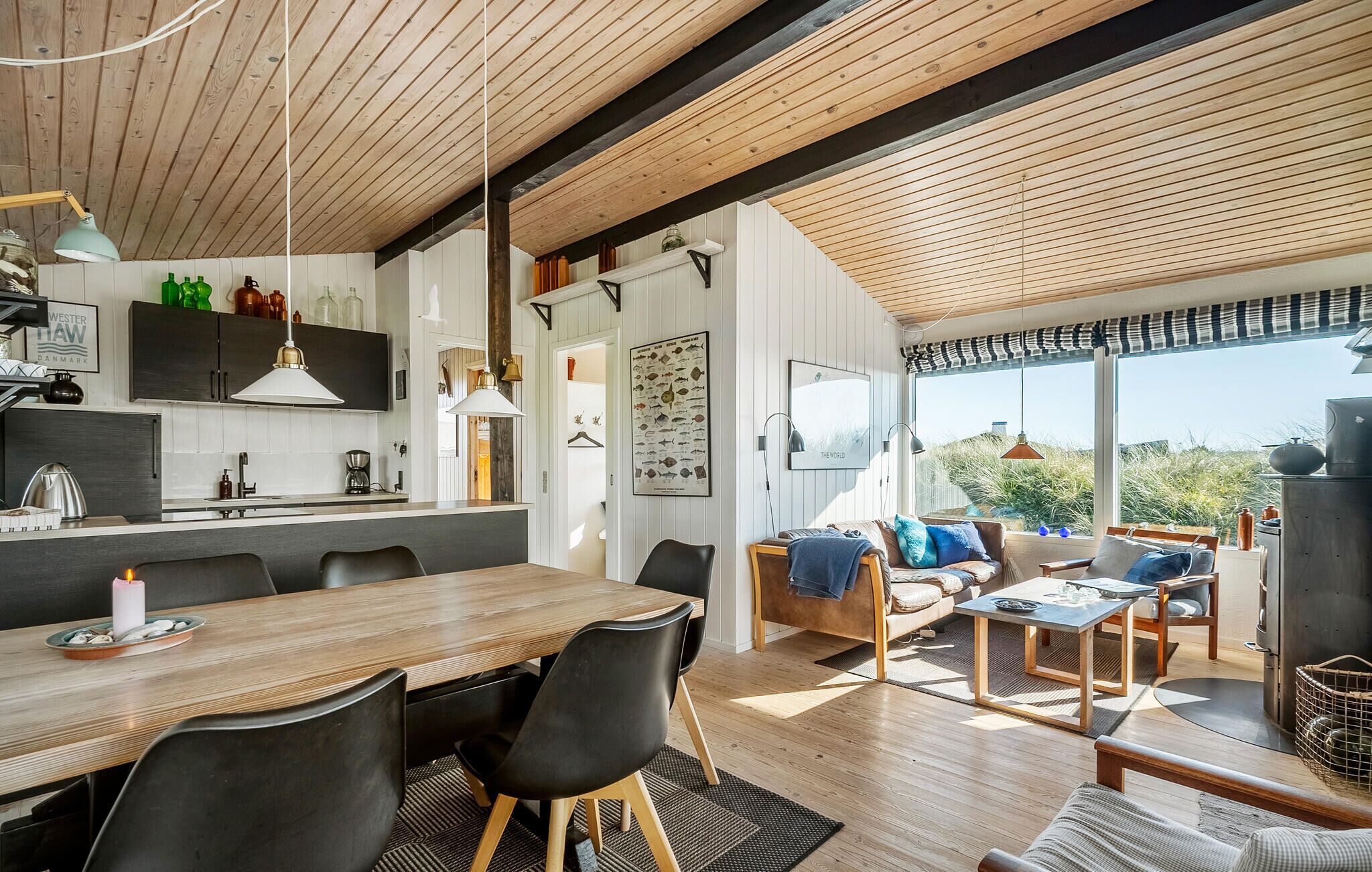 A modern kitchen with wooden beams, a dining area with a large table and chairs, and a cozy seating area with a sofa and cushions.