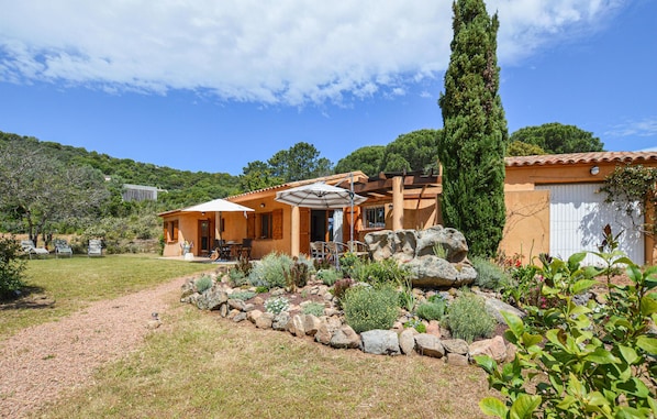 Eine mediterran gestaltete Villa mit Terrasse, Gartenmöbeln und einem Garten mit Steinen und Pflanzen.