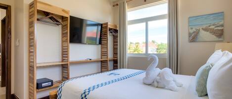 A hotel room with a bed, a TV mounted on the wall, a window with curtains, and a painting on the wall.