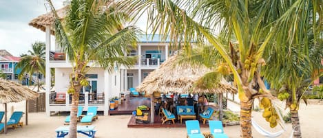 A beachside resort with lounge chairs, palm trees, and a thatched-roof bar area.