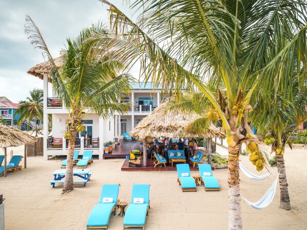 Un complexe hôtelier en bord de mer, doté de chaises longues, de palmiers et d’un espace bar à toit de chaume.