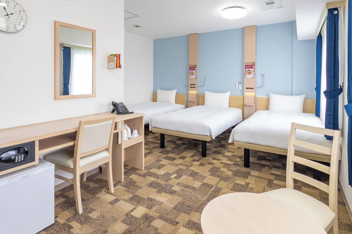 A hotel room with two single beds, a desk with a telephone, a small refrigerator, and a mirror.