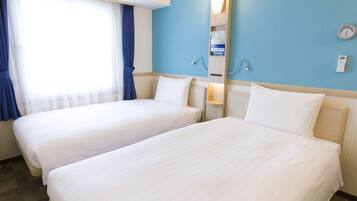A hotel room with two beds, a window with curtains, a wall-mounted clock, and a shelf with amenities.