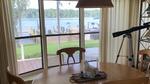 A dining area with a round wooden table, four chairs, a hanging lamp, and a view of a lake with boats. - Waterfront property! (Welaka)