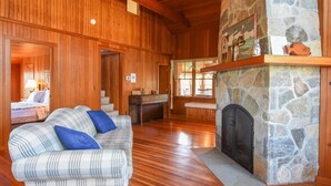 A cozy room with a stone fireplace, wooden walls, and a plaid sofa. - Steps to Nauset Beach, Private Yard! (Orleans)