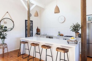 A modern kitchen with a white island, bar stools, hanging pendant lights, and a large mirror.