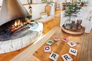 A cozy living room with a fireplace, a white sofa, and a wooden coffee table with Scrabble tiles. - The Deck Sorrento (Sorrento)