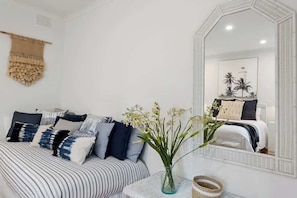 A bedroom with a bed, a bedside table with a vase, a mirror, and a wall hanging. - The Deck Sorrento (Sorrento)