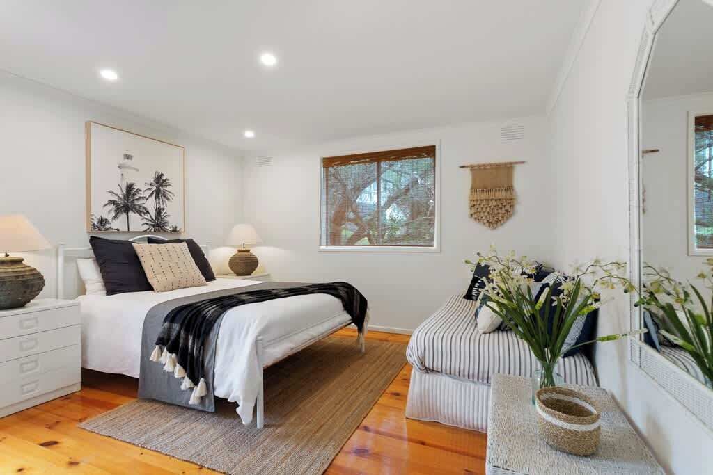 A bedroom with a bed, bedside table, lamp, and a window with a view.