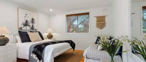 A bedroom with a bed, bedside table, lamp, and a window with a view.