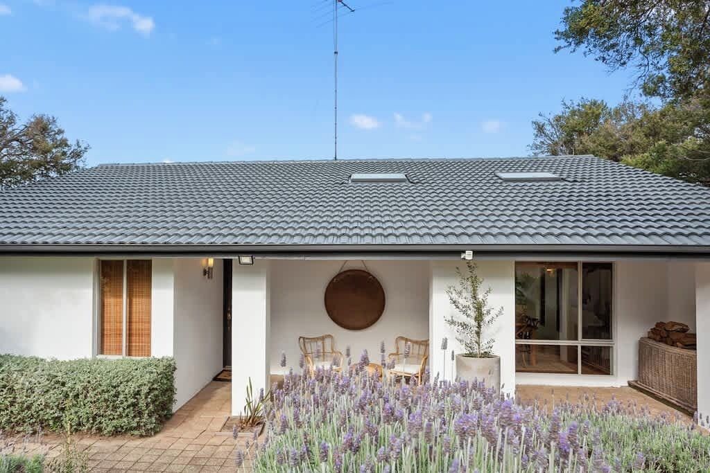 A house with a tiled roof, a covered porch with seating, and a garden with lavender.