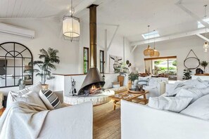 A spacious living room with a fireplace, white sofas, and a large window.