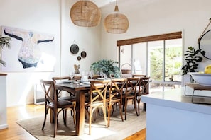 A dining area with a wooden table and chairs, a large window with a view, and a hanging rattan light fixture. - The Deck Sorrento (Sorrento)