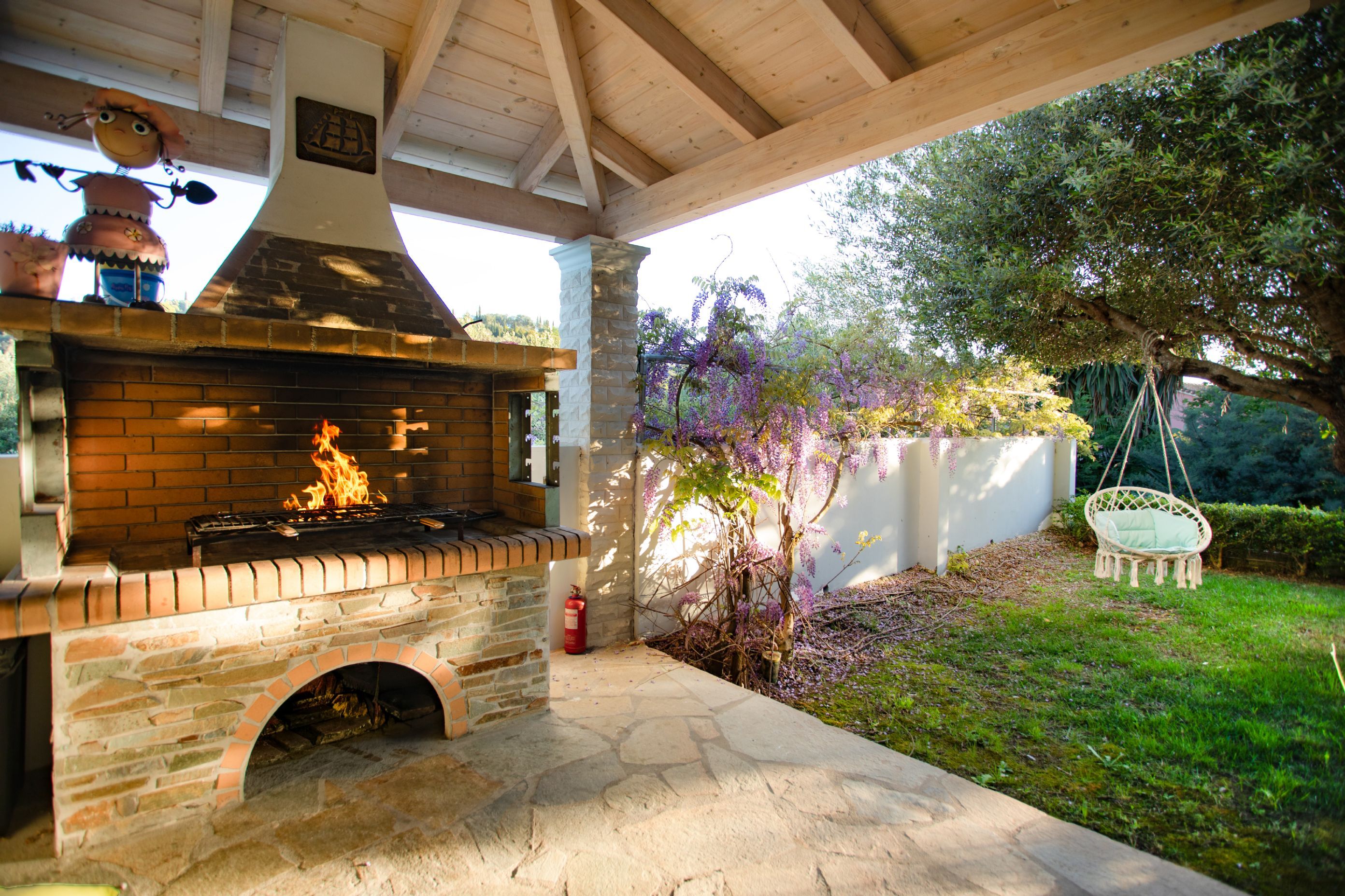 An outdoor brick barbecue grill with a chimney, under a wooden pergola.
