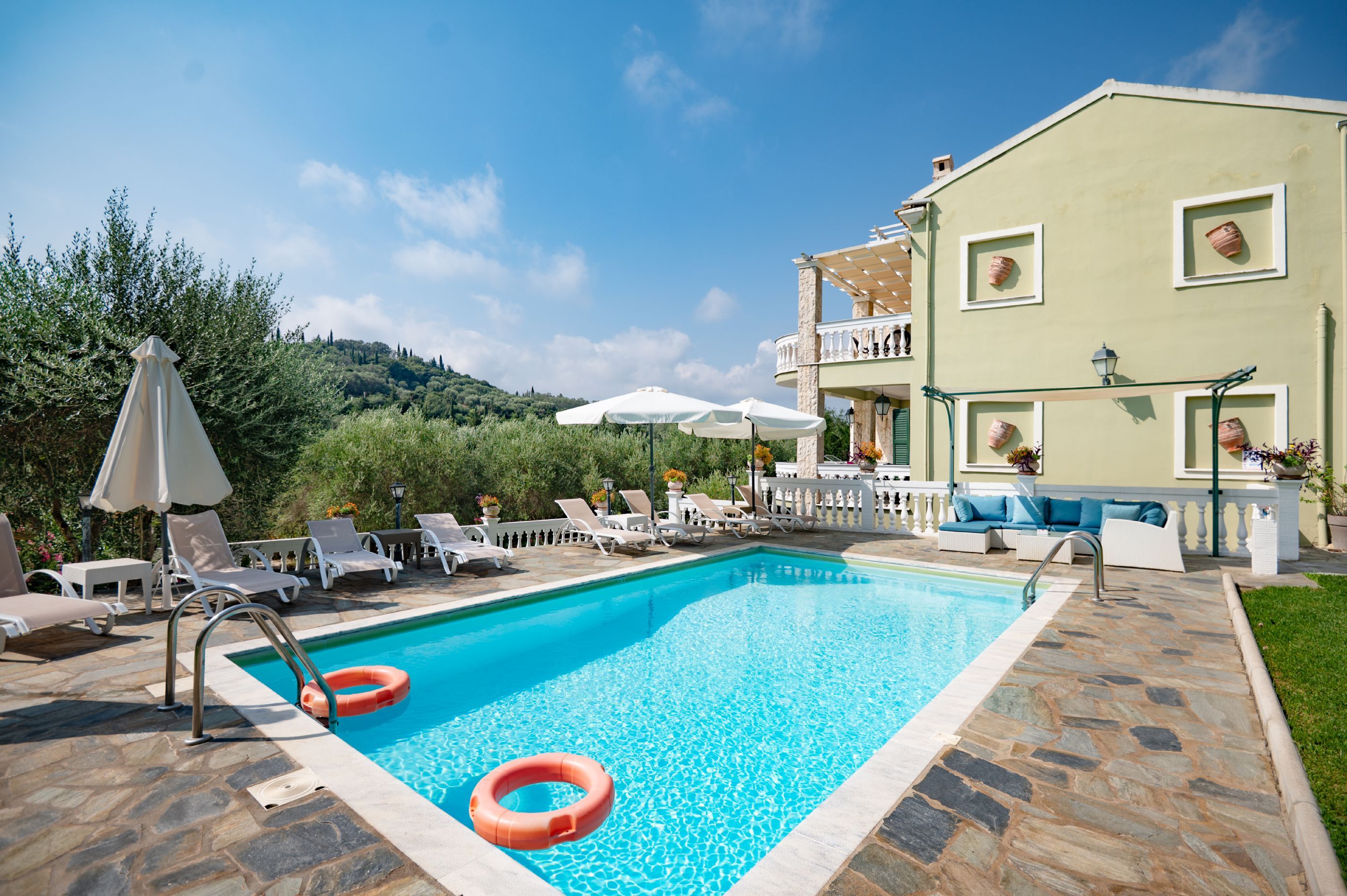 Ein Schwimmbecken mit Liegestühlen und Sonnenschirmen, umgeben von einem Gebäude mit Balkon und Blumentöpfen.
