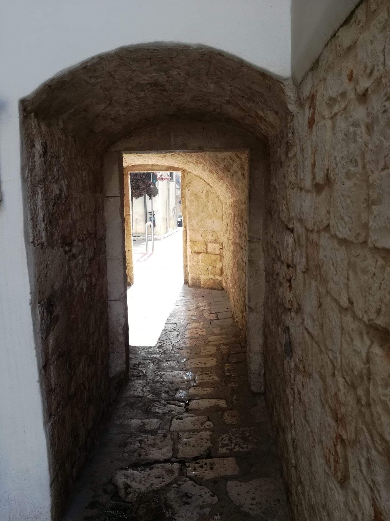 Un étroit couloir en pierre, dont le sol est irrégulier et accidenté, mène à un espace ouvert.