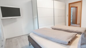 Un dormitorio con cama, televisor montado en la pared y puerta corredera.