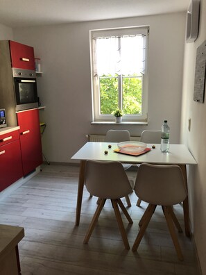 Keittiössä on ruokapöytä, tuoleja, punainen kodinkone ja ikkuna, josta avautuu näkymä vehreään maisemaan.