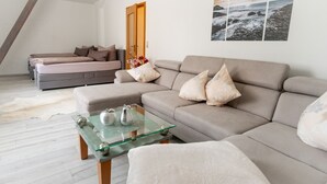 Una sala de estar moderna con un sofá, una mesa de centro de vidrio y una cama al fondo.