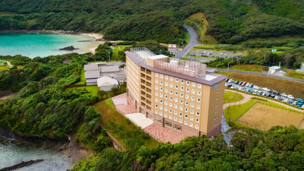 A hotel with multiple floors, a parking lot, and a view of a coastal area with greenery and a beach.