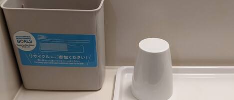 Un bote de basura con etiqueta de reciclaje y una taza blanca sobre una bandeja.