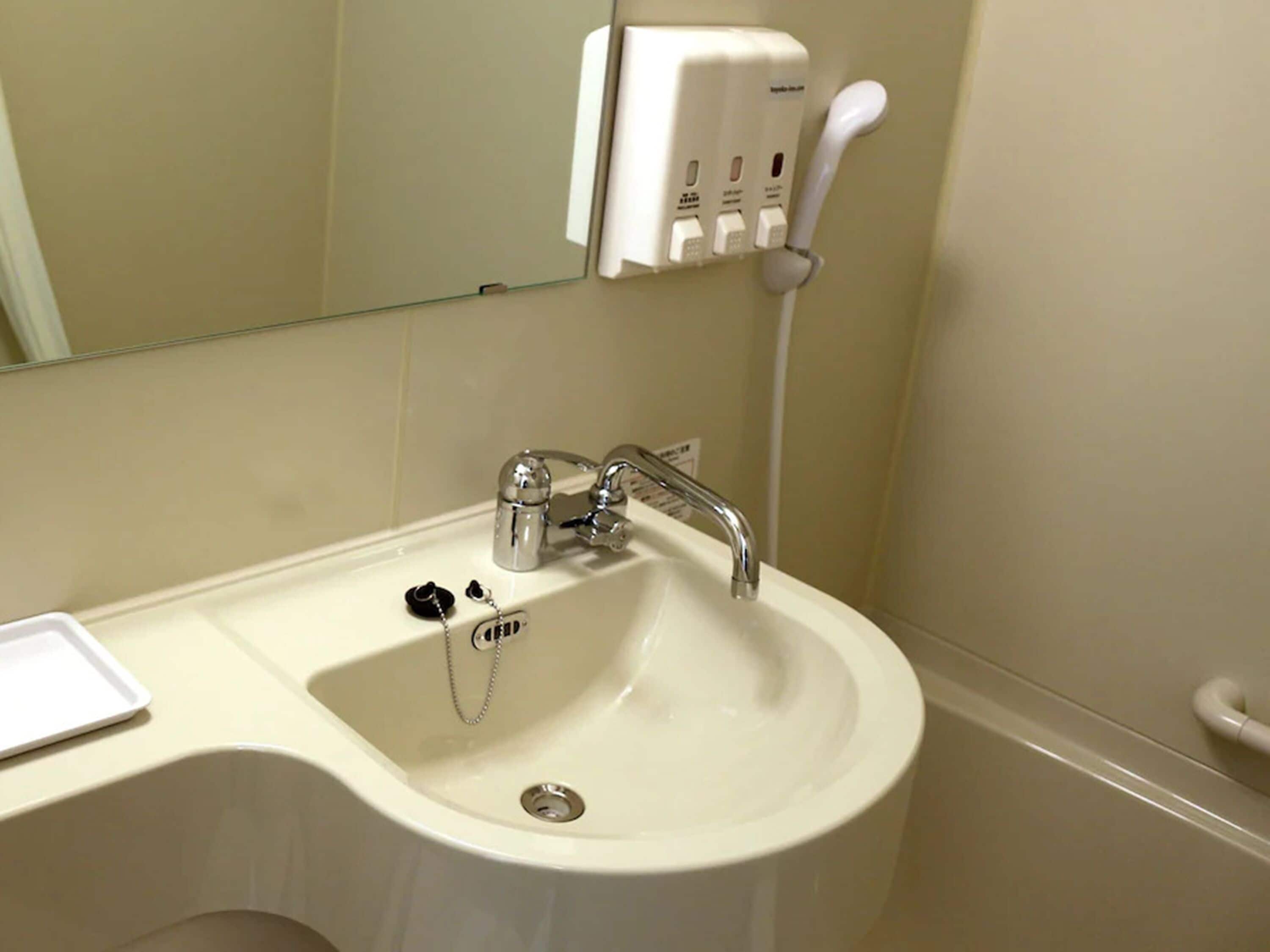 Un lavabo blanc dans une salle de bain, avec un robinet chromé, un distributeur de savon et un miroir au-dessus.
