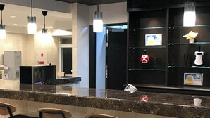 A modern bar area with marble countertops and black chairs. There are multiple light fixtures above the bar, and a digital screen displaying information.