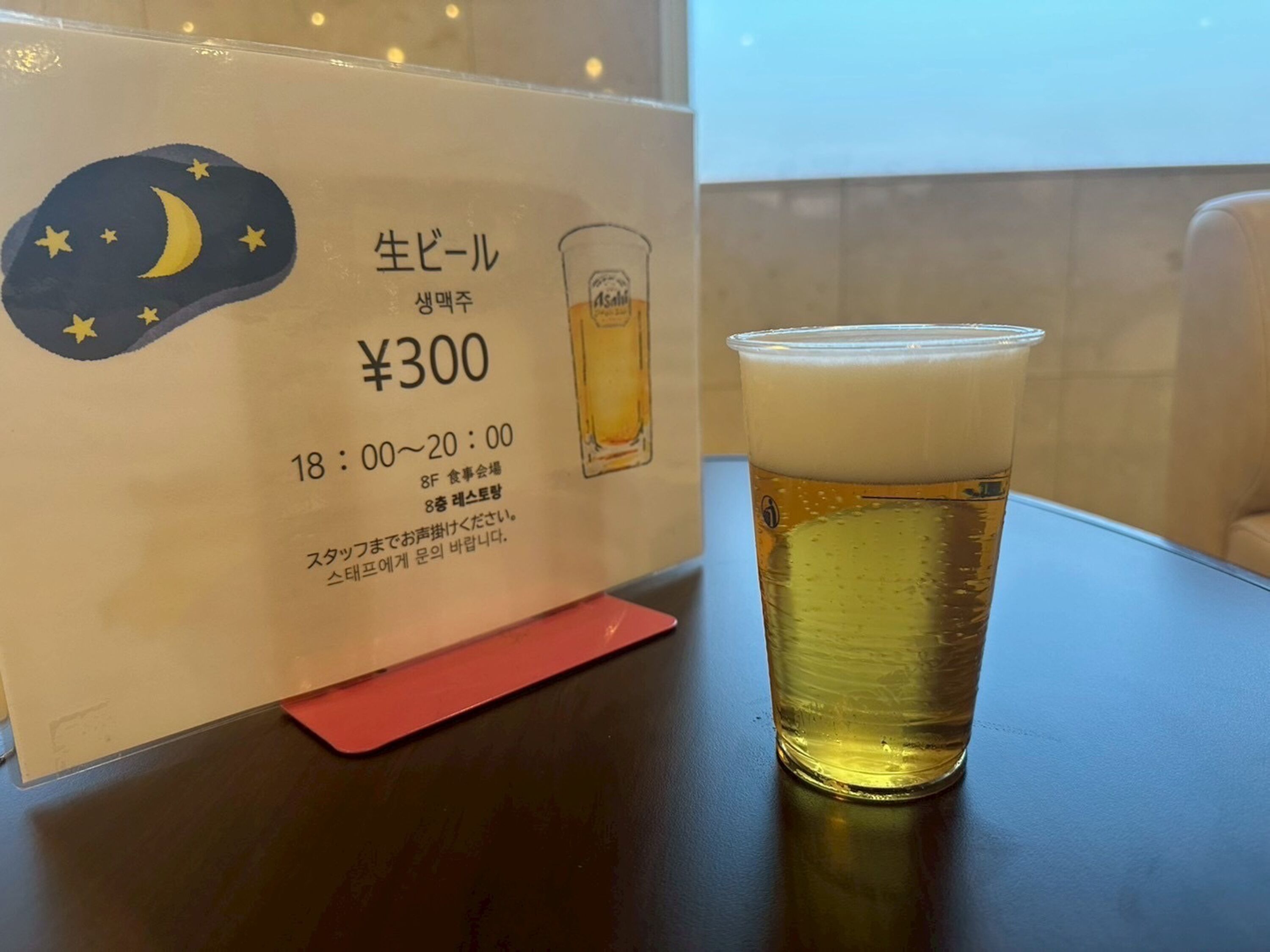 A glass of beer on a table with a sign indicating a price of ¥300 and operating hours from 18:00 to 20:00.