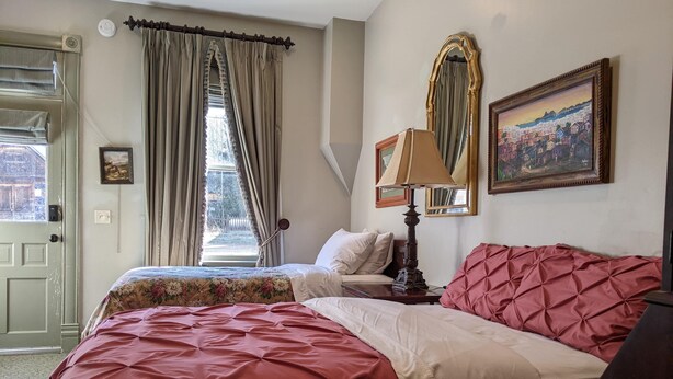 Un dormitorio con dos camas, una ventana con cortinas, una lámpara y un cuadro en la pared.