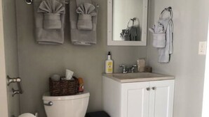 Un baño con inodoro, lavamanos y espejo. Hay toallas colgadas en la pared y una cesta sobre el inodoro.