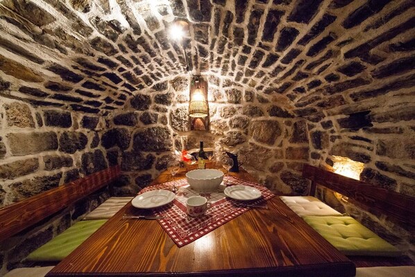 Un comedor con paredes de piedra y una mesa de madera dispuesta para dos personas, con un camino de mesa estampado y un candelabro.