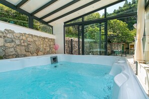 Una piscina interior moderna con paredes de piedra y puertas de cristal, rodeada de follaje.