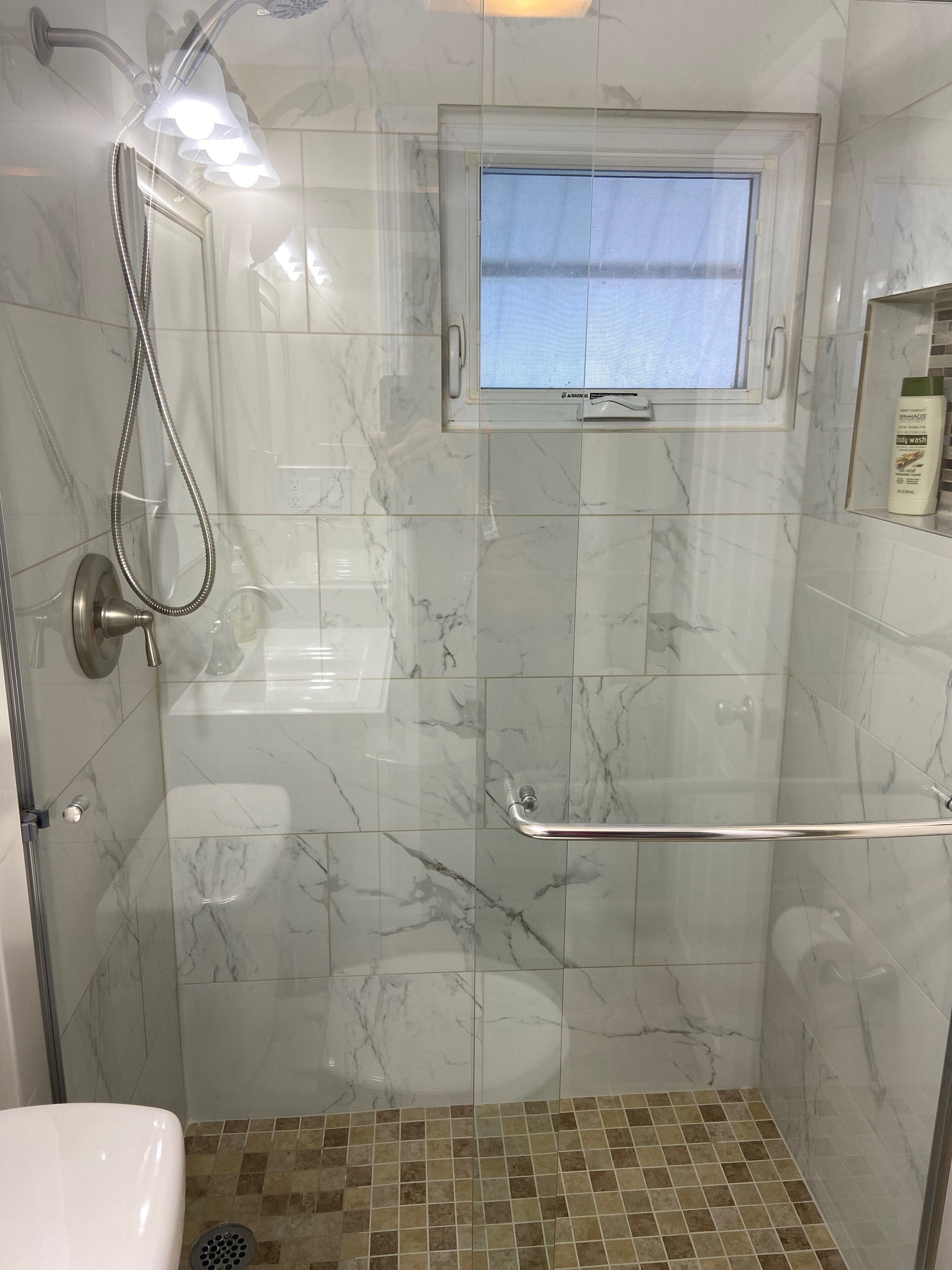 A bathroom with a shower, a window, and a handrail.