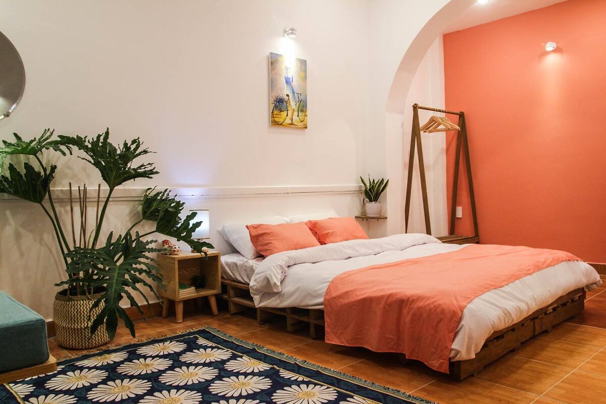 A bedroom with a bed, two bedside tables, a hanging chair, and potted plants.