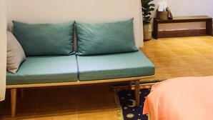 Ein Zimmer mit einem grünen Sofa, einem kleinen Gemälde an der Wand, einer hängenden Ampel und einer Holzbank.