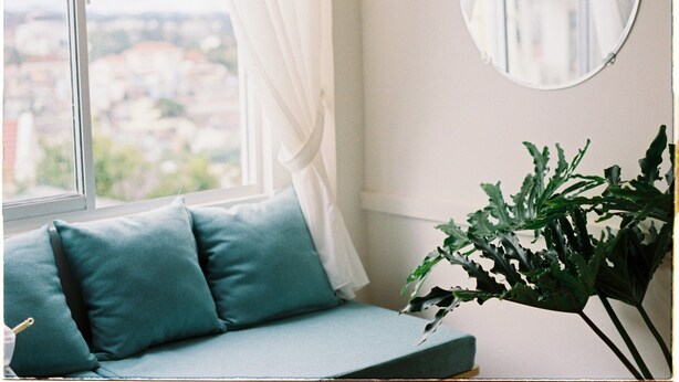 Ein Zimmer mit Blick auf eine Stadtansicht durch ein Fenster, einem runden Spiegel an der Wand und einer Pflanze auf einem Tisch.
