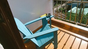 Ein blauer Stuhl auf einem Balkon mit Metallgeländer und Blick auf Grünflächen sowie Gebäude im Hintergrund.