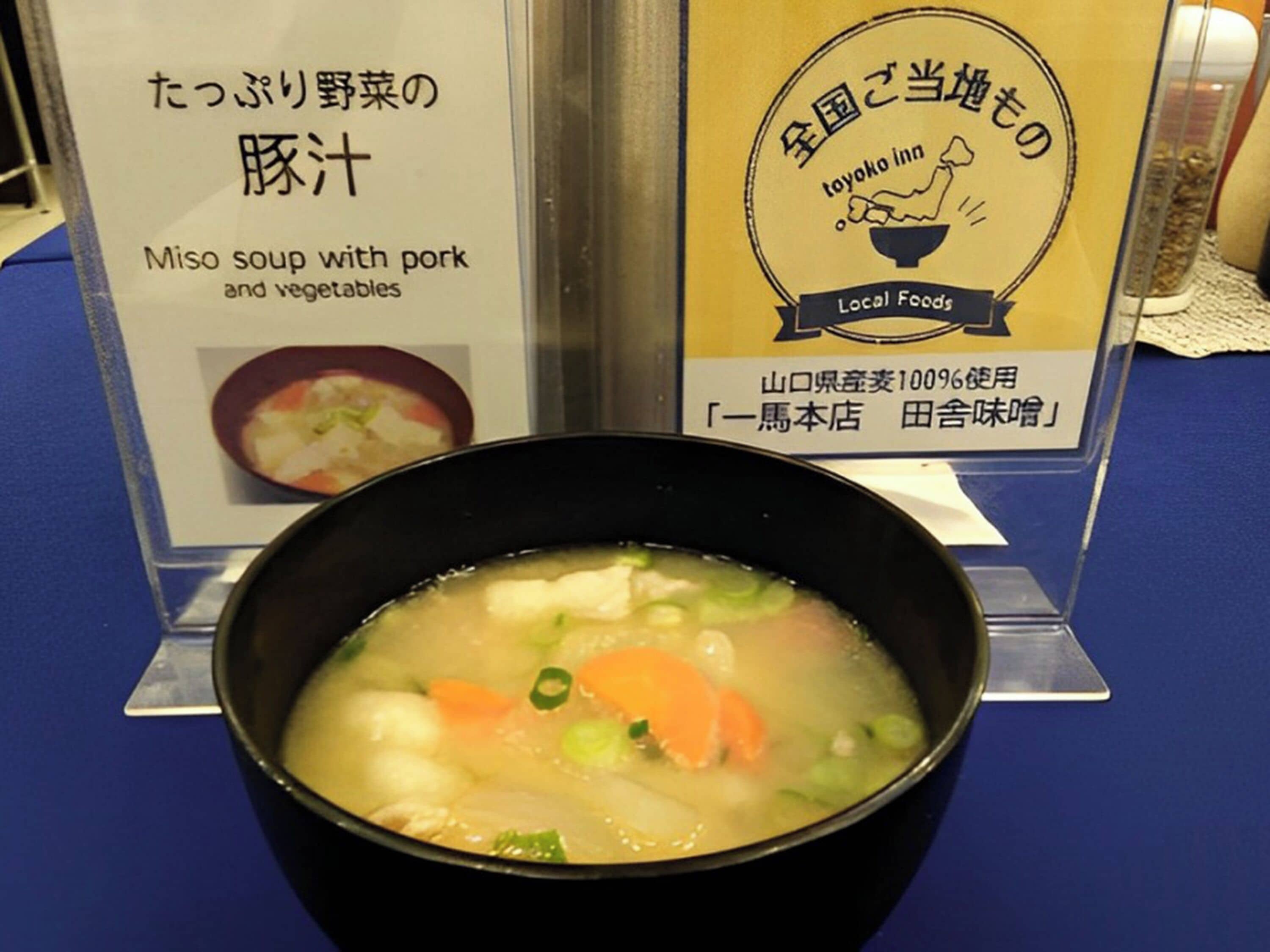 Un bol de soupe miso aux légumes et au porc, une enseigne indiquant le menu et une enseigne « Toyoko Inn ».